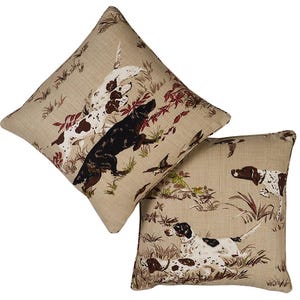 May include: Two beige throw pillows with a brown and white hunting dog pattern. The pillows feature a brown and white dog, a black and white dog, and a brown and white dog.