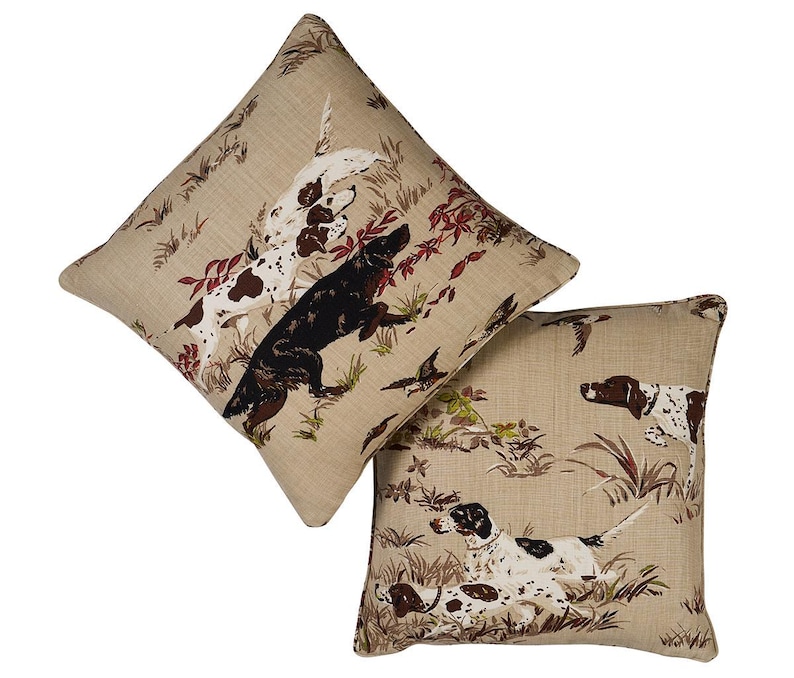 May include: Two beige throw pillows with a brown and white hunting dog pattern. The pillows feature a brown and white dog, a black and white dog, and a brown and white dog.