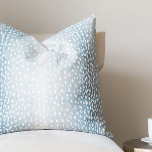 May include: A cushion with a blue and white spotted design. The cushion is on a cream-coloured chair. A white teacup and saucer are on a small, gold-coloured side table.