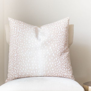 May include: A light pink throw pillow with a white deer print pattern.