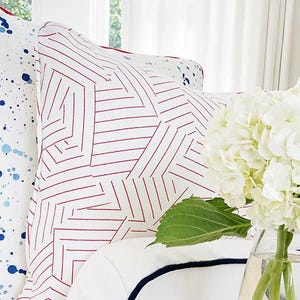 May include: White and red geometric patterned throw pillow with a white background and red lines forming a geometric pattern.