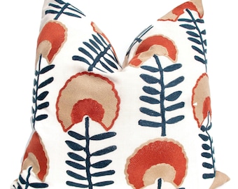 May include: A white pillow with a floral pattern in shades of rust, beige, and navy blue. The pillow features a repeating design of stylized flowers with rounded petals and leaves.