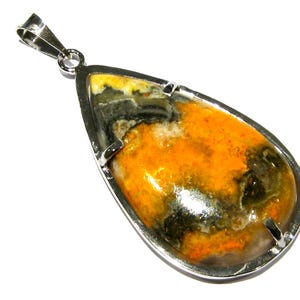 Puede incluir: Un colgante en forma de lágrima con una piedra amarilla, negra y gris engastada en un bisel de plata.
