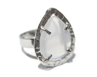 May include: A silver ring with a pear-shaped, light-colored stone. The stone is set in a textured silver bezel. The ring band is a simple, polished silver. The ring is on a white background.