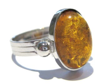May include: A silver ring with a large oval amber stone. The amber is a deep orange color and has a lot of inclusions.