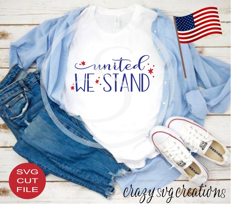 May include: A white t-shirt with the text "united we stand" in blue with red stars. The shirt is laid out on a wooden surface with blue jeans, a light blue shirt, and white sneakers.