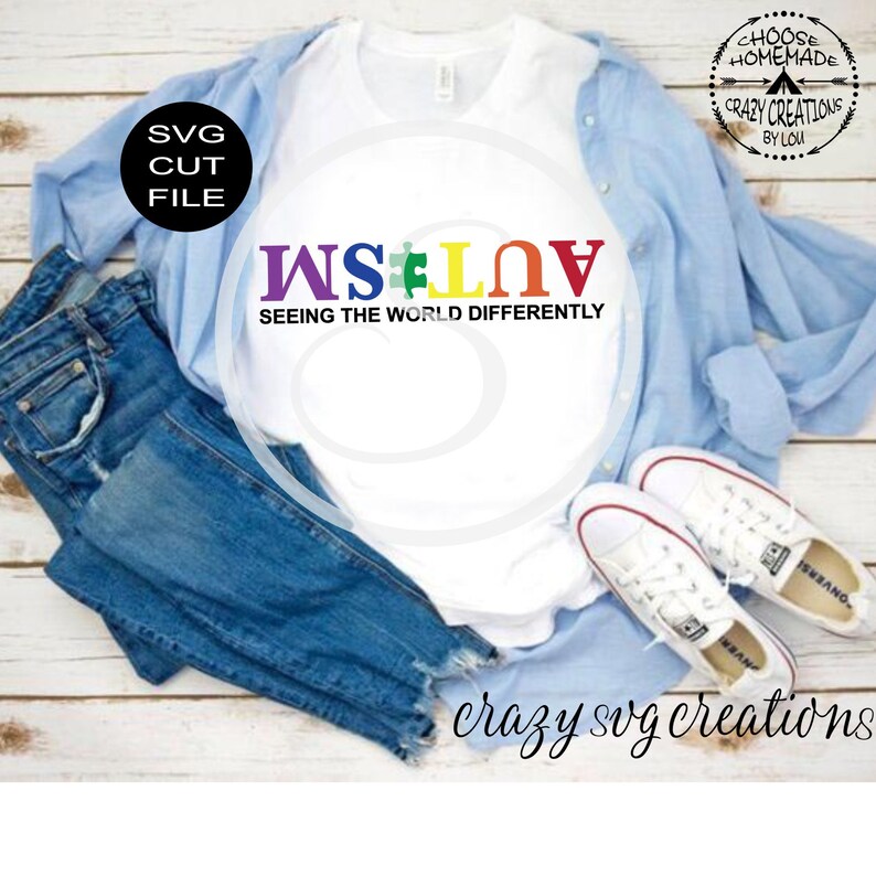 Puede incluir: Una camiseta blanca con el texto "WS#LOV" en colores arco&iacute;ris y la frase "SEEING THE WORLD DIFFERENTLY" en texto negro. La camiseta est&aacute; colocada sobre una superficie de madera con unos vaqueros azules, una camisa azul claro y unas zapatillas blancas.