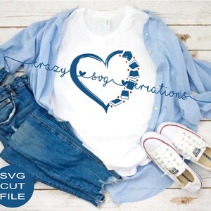 May include: A white t-shirt with a blue heart design featuring books and the text "crazy svg creations". The shirt is displayed on a wooden surface with blue jeans and white sneakers.