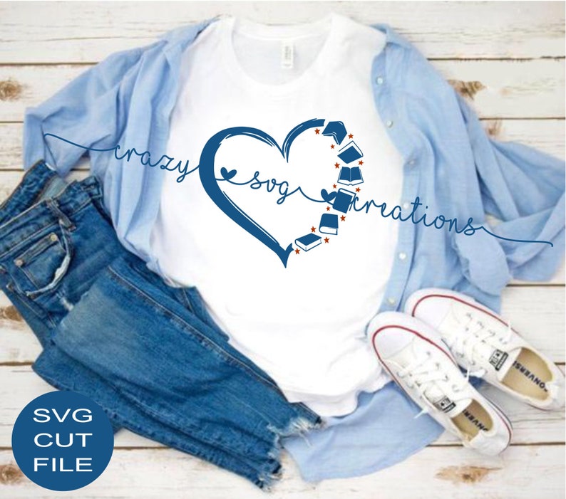 May include: A white t-shirt with a blue heart design featuring books and the text "crazy svg creations". The shirt is displayed on a wooden surface with blue jeans and white sneakers.