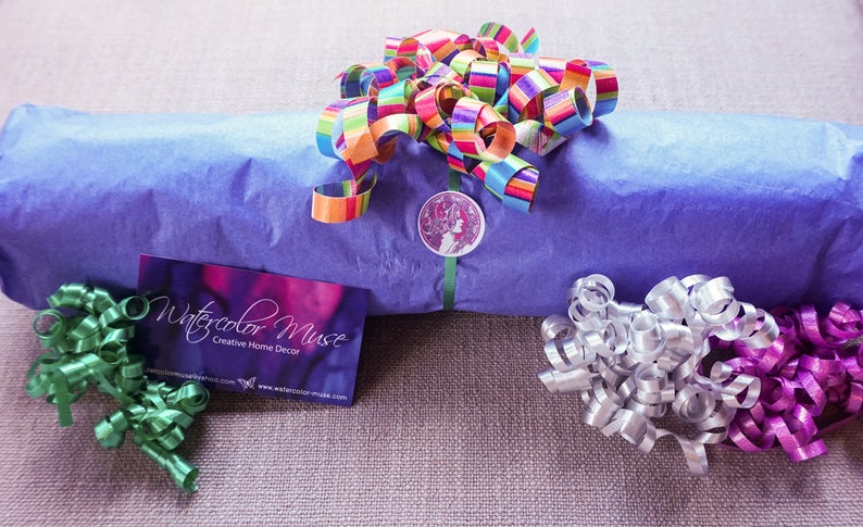 May include: A blue gift wrapped in tissue paper with a colorful ribbon and a sticker that says "Watercolor Muse Creative Home Decor" and the website www.watercolor-muse.com. The gift is surrounded by green, silver, and purple curling ribbon.