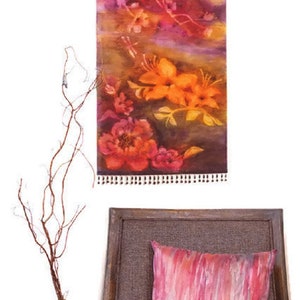 May include: A wall tapestry with a floral design featuring orange, pink, and purple flowers. The tapestry is hanging on a wooden branch and has a fringe border.