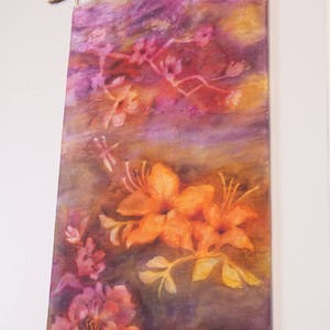 May include: A colorful wall hanging with a floral design. The hanging features a variety of flowers in shades of pink, orange, and yellow. The hanging is accented with a beaded fringe.