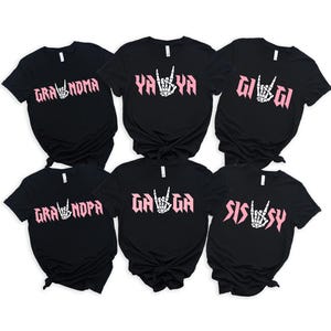 May include: Six black t-shirts with pink text and a hand symbol. The shirts read "Gra'noma", "Ya'Ya", "Gi'Gi", "Gra'npa", "Ga'Ga", and "Sissy".