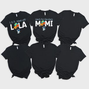 May include: Black t-shirts with white text and colourful graphics. One shirt says "1, 2, 3... blast off!" with "LOLA" below, and an astronaut holding balloons. Another says "reach for the stars" with "MOMI" below.