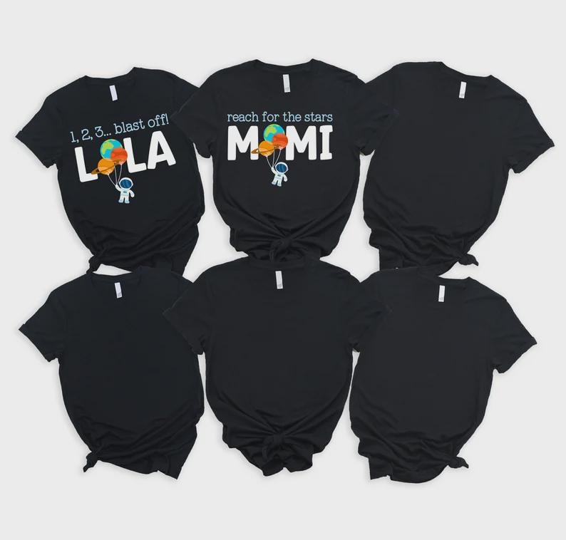 May include: Black t-shirts with white text and colourful graphics. One shirt says "1, 2, 3... blast off!" with "LOLA" below, and an astronaut holding balloons. Another says "reach for the stars" with "MOMI" below.
