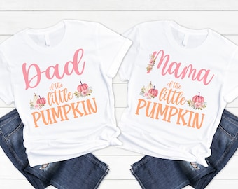 May include: Two white t-shirts with the text "Dad of the little pumpkin" and "Mama of the little pumpkin" in pink and orange lettering. Each shirt features a small pumpkin graphic with floral accents.