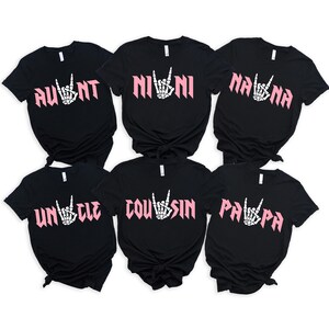 May include: Six black t-shirts with white text and pink rock and roll hand symbols. The shirts say "Aunt", "Nini", "Nana", "Uncle", "Cousin", and "Papa".