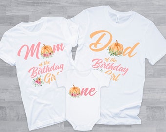 Może przedstawiać: Białe koszulki z napisem "Mom of the Birthday Girl" i "Dad of the Birthday Girl" z grafiką dyni. Biały śpioszek z napisem "One" i grafiką dyni.