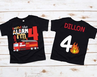 Puede incluir: Dos camisetas negras con temática de camión de bomberos. La camiseta delantera dice "Sound the Alarm I'm 4" con un camión de bomberos rojo y una boca de incendios. La camiseta trasera dice "Dillon" en texto rojo y tiene un número blanco "4" con un gráfico de llama.