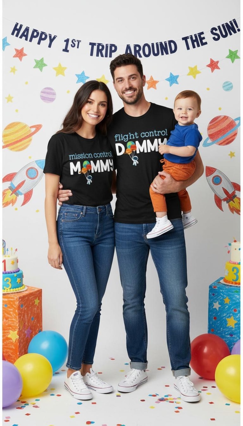 May include: A family of three wearing matching black t-shirts with space-themed graphics and text. The shirts say "Mission Control Mommy" and "Flight Control Daddy." The background features a space-themed banner and decorations.