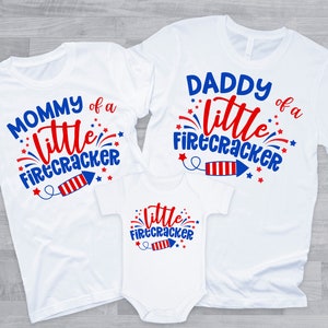 May include: Three white t-shirts with red, white, and blue text and graphics. The shirts say "Mommy of a little firecracker", "Daddy of a little firecracker", and "little firecracker".
