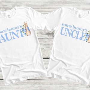 Puede incluir: Dos camisetas blancas con texto azul y una ilustraci&oacute;n de Peter Rabbit. Una camiseta dice "some bunny's AUNT" y la otra dice "some bunny's UNCLE".