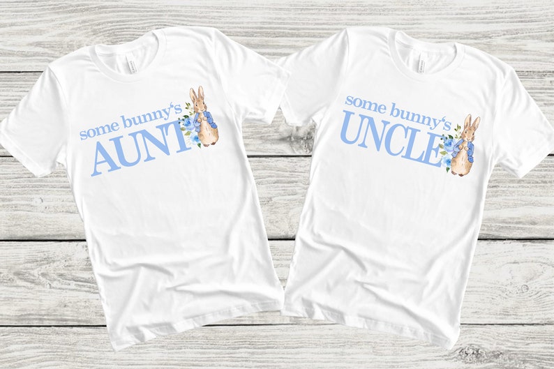 Puede incluir: Dos camisetas blancas con texto azul y una ilustraci&oacute;n de Peter Rabbit. Una camiseta dice "some bunny's AUNT" y la otra dice "some bunny's UNCLE".