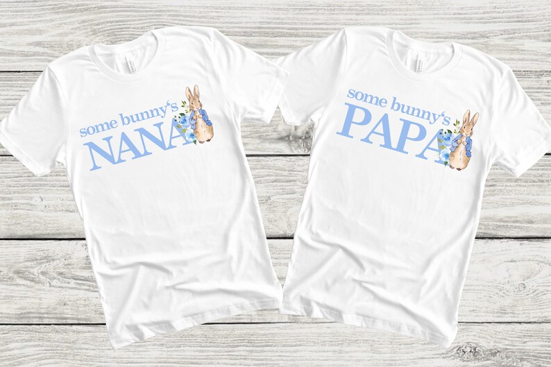 Puede incluir: Dos camisetas blancas con texto azul y un conejito de dibujos animados. El texto de la camiseta de la izquierda dice "some bunny's NANA" y el texto de la camiseta de la derecha dice "some bunny's PAPA".
