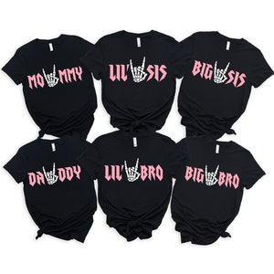 May include: Six black t-shirts with pink text and a skeleton hand making a rock and roll sign. The shirts say "Mommy", "Lil' Sis", "Big Sis", "Daddy", "Lil' Bro", and "Big Bro".