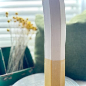 May include: A tall, hexagonal ceramic vase with a gradient of light pink to yellow. The vase is sitting on a silver turntable.