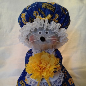 May include: A handmade sock monkey doll wearing a blue and yellow University of Pittsburgh shower cap and dress with white lace trim. The doll is holding a yellow flower.