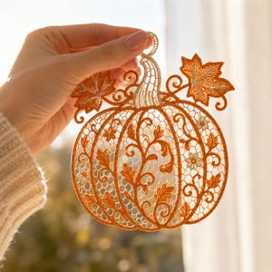 May include: An orange pumpkin-shaped ornament crafted from intricate lace embroidery. The design features detailed leaf patterns, swirling vines, and small flower motifs throughout the body, topped with a stem and two prominent maple-like leaves.