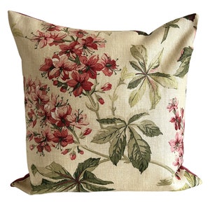 Pode incluir: Uma almofada bege com um padrão floral com flores vermelhas e rosas e folhas verdes.