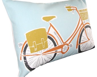 May include: A light blue pillow with a printed design of an orange bicycle with a brown leather bag and a wicker basket. The bicycle has white wheels and a white handlebar.