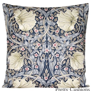 Könnte beinhalten: Quadratisches Zierkissen mit floralem Muster. Das Design zeigt große cremefarbene Blüten, kleine rosa Blüten und graublaue Blätter und Stiele auf einem dunkelblauen Hintergrund. Der Text "Pretty Cushions" befindet sich unten rechts.