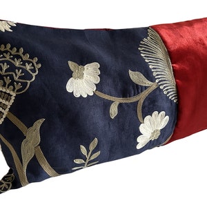 May include: Decorative lumbar pillow with a navy blue floral embroidered design and a red satin finish. The pillow features a detailed gold and white floral pattern, adding a touch of elegance to any room.