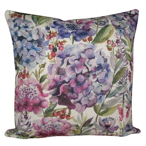 Puede incluir: Una almohada cuadrada con un patrón floral. La almohada presenta un diseño de acuarela de flores moradas, rosas y azules sobre un fondo blanco.