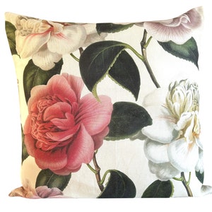 Puede incluir: Cojín cuadrado con diseño floral. Presenta ilustraciones grandes y detalladas de flores de camelia rosas y blancas con hojas verdes sobre un fondo blanco. Las flores están representadas en un estilo de ilustración botánica vintage.