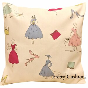 May include: A cream-colored pillowcase with a repeating pattern of women in dresses, shoes, and handbags. The text "Pretty Cushions" is printed in the bottom right corner.