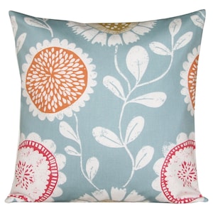 Puede incluir: Una almohada azul con un patrón floral blanco y naranja. Las flores son estilizadas y tienen una forma circular con un círculo naranja central y pétalos blancos.