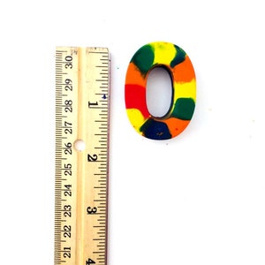 May include: A colorful, multi-colored,  wax crayon number zero. The number is approximately 1 inch tall and is made of a variety of colors including red, orange, yellow, green, and blue.