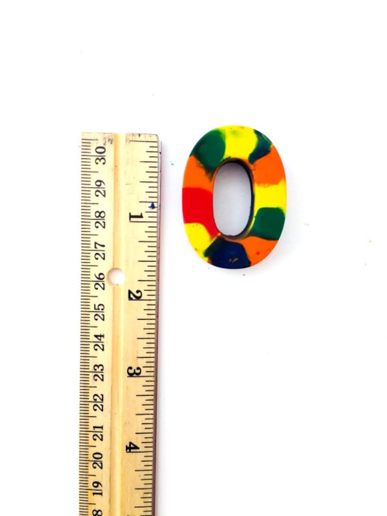 May include: A colorful, multi-colored,  wax crayon number zero. The number is approximately 1 inch tall and is made of a variety of colors including red, orange, yellow, green, and blue.