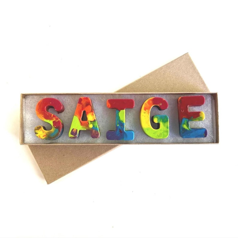 May include: A set of colorful crayon letters spelling the name "SAIGE" in a brown cardboard box.