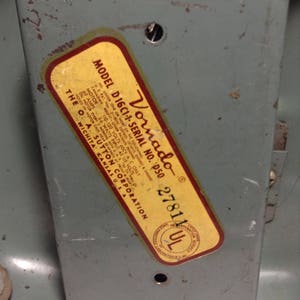 Puede incluir: Una etiqueta amarilla y roja con el texto "Vornado Model D16C1-1-Serial No. D50 27811 UL" en una superficie de metal gris. La etiqueta incluye informaci&oacute;n sobre el voltaje, la potencia y otras especificaciones del producto.