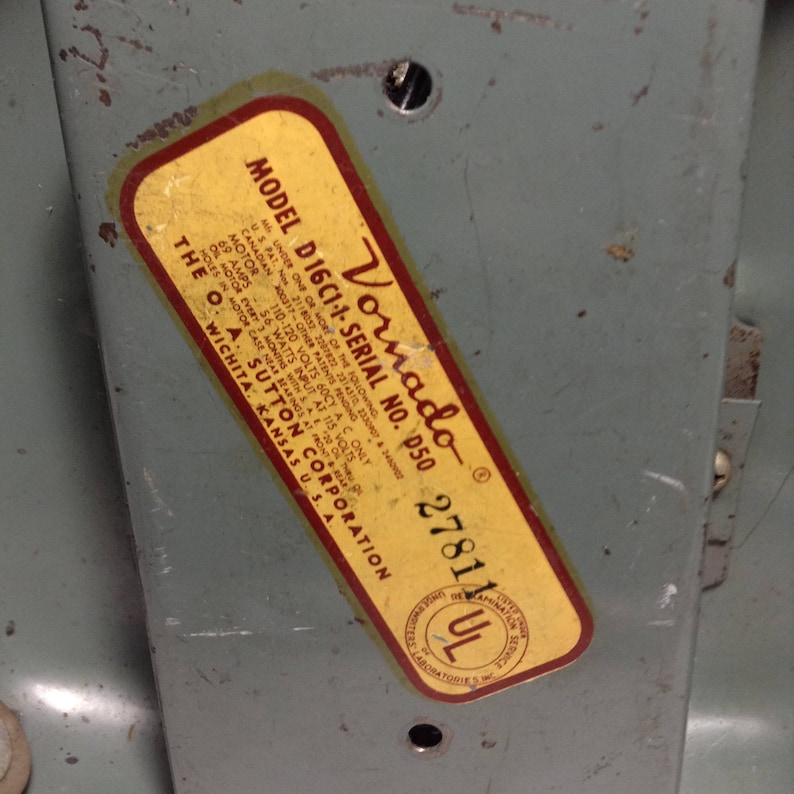 Puede incluir: Una etiqueta amarilla y roja con el texto "Vornado Model D16C1-1-Serial No. D50 27811 UL" en una superficie de metal gris. La etiqueta incluye informaci&oacute;n sobre el voltaje, la potencia y otras especificaciones del producto.