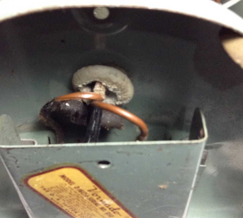 Puede incluir: Primer plano del interior de un ventilador de techo con un cable marr&oacute;n y una toma de cer&aacute;mica blanca. El ventilador est&aacute; etiquetado como "Tornado" y tiene un n&uacute;mero de modelo.