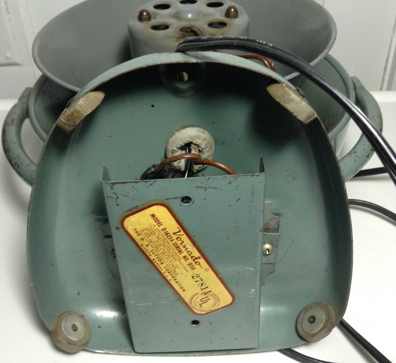 Puede incluir: Un ventilador Vornado vintage con un cuerpo de metal azul claro y un cable negro. El ventilador tiene una etiqueta en la parte inferior que dice "Vornado Model D16C1 Serial No. 050 278141 UL".