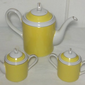 May include: A yellow and white porcelain tea set with a teapot, creamer, and sugar bowl. The set has a gold trim and a yellow band around the middle of each piece.