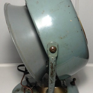 Puede incluir: Un calentador el&eacute;ctrico vintage de color azul claro con un asa de metal y una base redonda. El calentador tiene una rejilla de metal y un cable.