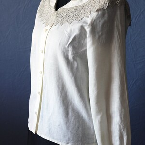 May include: A white long-sleeved button-up shirt with a large, lacy collar. The collar is white with a delicate, intricate design.